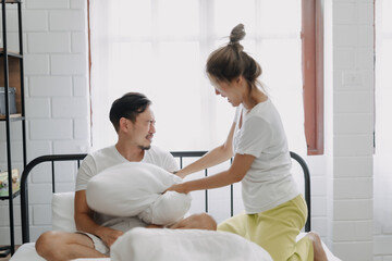Obraz premium Asian wife and husband playing pillow fight funny and laugh on the bed.