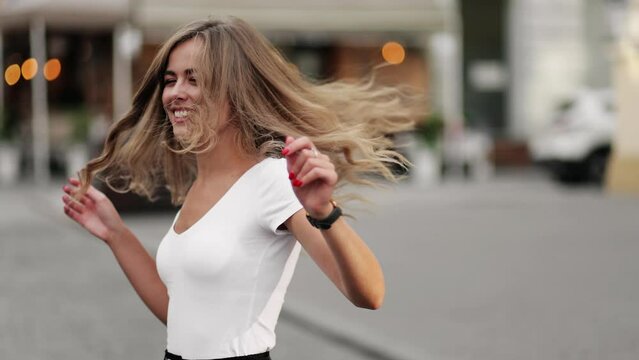 Portrait of young beautiful blonde woman spinning in the center of a city Attractive female with flying hair outdoors Beautiful girl shakes hair in slow motion
