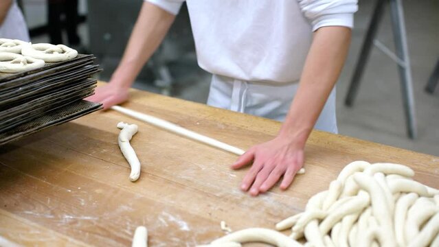 Baker forming pretzel from dough in the bakery bakehouse early in the morning