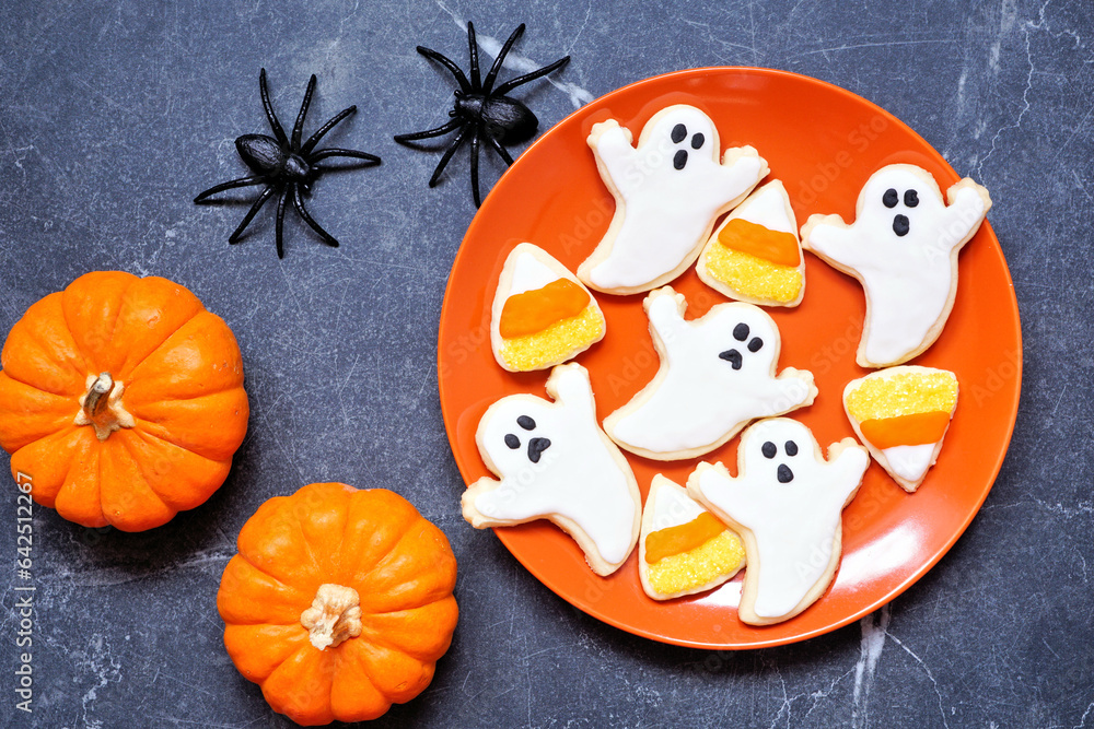 Poster plate of halloween ghost and candy corn cookies. above view table scene on a dark stone background.