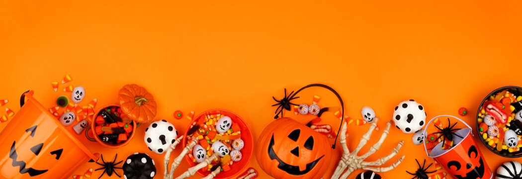 Halloween trick or treat bottom border with jack o lantern pails and an assortment of candy. Top view on an orange banner background with copy space.