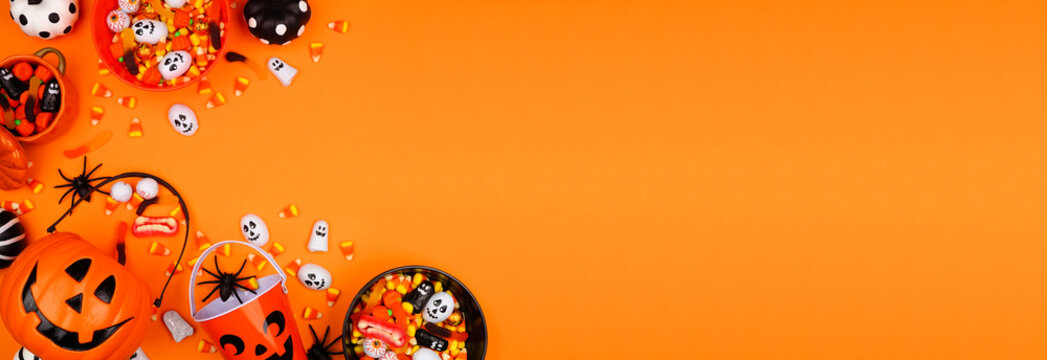Halloween trick or treat corner border with jack o lantern pails and a variety of candy. Top down view on an orange banner background with copy space.