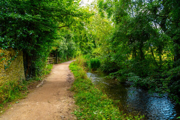 A scenic shady dirt path walkway along the River Eye in the English countryside at the Cotswold...