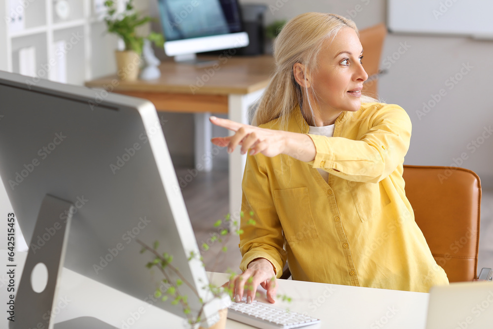 Poster mature female programmer working with computer at table in office