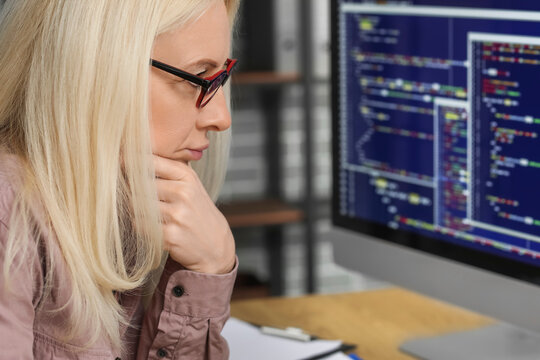 Mature female programmer working with computer at table in office, closeup