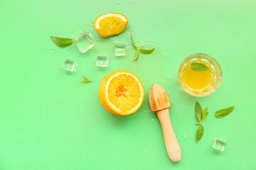Orange with juicer, glass, ice cubes and mint on green background