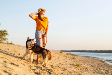 Woman in hat and sunglasses with her dog enjoying sunset on the beach
