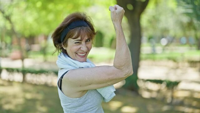 Middle age woman wearing sportswear doing strong gesture with arm at park