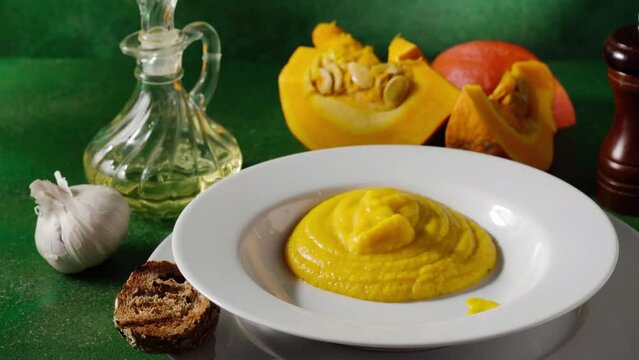Pouring hot and creamy pumpking soup in a plate on green background