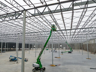construction workers working on roof trusses of a warehouse on a forklift