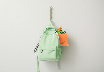 School backpack with different stationery hanging on light wall