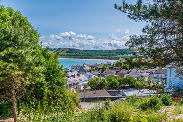 A view past trees over the harbour and buildings in the West Wales town of New Quay in summertime