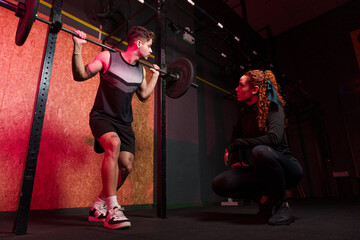 Personal trainer instructing student in barbell squats at gym