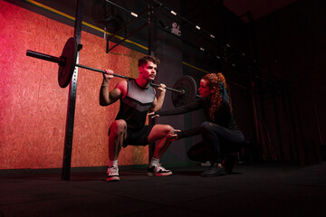 Personal trainer instructing student in barbell squats at gym