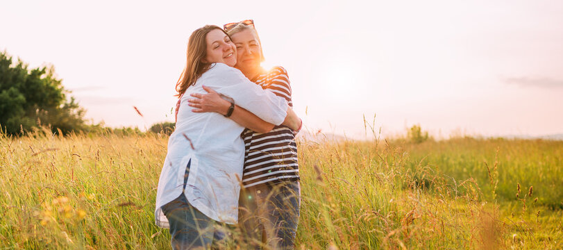Portrait of sincerely smiling young pregnant woman dressed in light summer clothes with mother in evening sunset hours. They are hugging tight. Woman's health, human in the nature concept image.