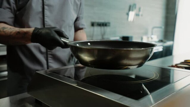 close-up of a chef placing a frying pan on an induction stove in a professional restaurant kitchen