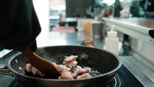 chef in a professional kitchen in a restaurant frying juicy chicken fillet in a pan close-up