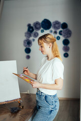 woman in a white t-shirt with an easel and brushes for painting.