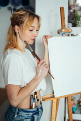 woman in a white t-shirt with an easel and brushes for painting.