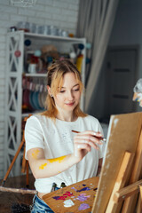 The artist paints in oils at the easel. In the hands of a palette and brush. White T-shirt and apron. Portrait. Creative person concept. 