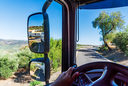 View from the cab of a truck of a narrow road and the rearview mirror where you can see the sharp turn of the tank trailer.
