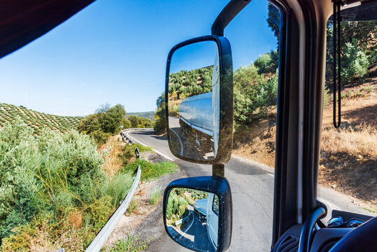 Rearview mirrors of a tanker truck driving along a narrow mountain road, occupying the entire road when cornering.