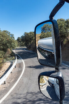 Rearview mirrors of a truck where you can see the sharp turn occupying the entire road of the tanker trailer on a narrow mountain road.