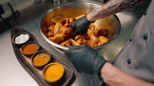 professional restaurant kitchen chef stirs chicken wings with spices in a bowl asian dish close-up