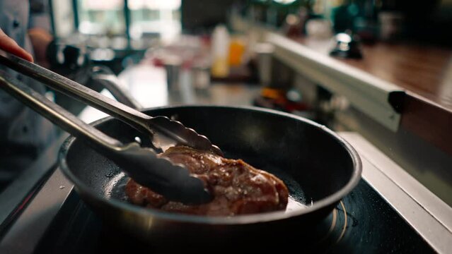 close-up of juicy duck breast with fried skin in a frying pan with butter the cook is frying the meat turning it over with tongs