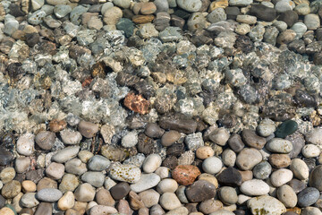 clear lake water flowing over large rounded pebbles in summer at a cove