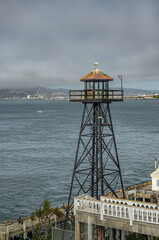 Fototapeta na wymiar San Francisco, CA, USA - July 12, 2023: Alcatraz Island east shore historic prison watchtower closeup. East bay shoreline on horizon under light gray sky