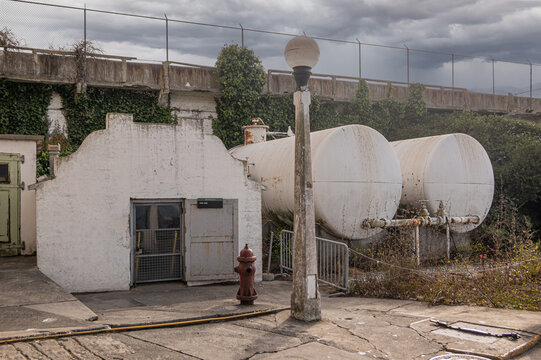 San Francisco, CA, USA - July 12, 2023: Small historic white morgue building closeup with 2 large tanks on side. Gray cloudscape and some green foliage