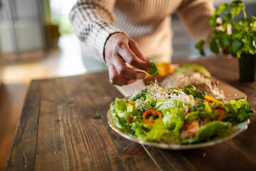 Middle aged woman preparing a healthy salad with organic fruits and vegetables at home and decorating a plate