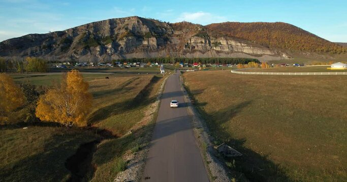 The car is moving along the road towards beautiful and picturesque rocks, aerial view. Autumn season. The drone follows the car. Southern Urals