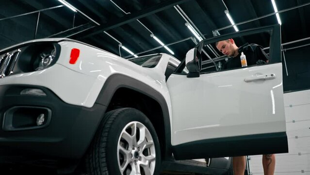 Close-up of a car wash worker using a plastic washing brush while cleaning the door card of a luxury car during the detailing process