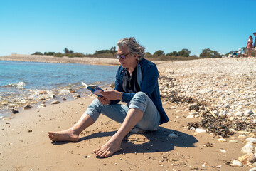 Fototapeta na wymiar A fifty-year-old man sitting by the seaside reading a book