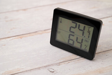 Digital indoor temperature and humidity monitor in a summer on a wooden table.