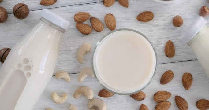Various vegan milk types, alternative milk made of nuts, almonds, cashew poured into glasses on white table, top table view, slow motion video clip, blank bottles with no label, non-dairy product