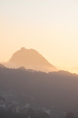 Rio de Janeiro, Brazil: city skyline with the Sugarloaf Mountain and Cable Car shrouded in fog after the dawn in the early morning sunlight seen from an high terrace on Copacabana beach