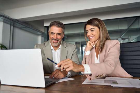 Female Professional Business Manager Consulting Older Indian Male Client Or Colleague Looking At Laptop Computer Technology Discussing Ebusiness Data Planning Corporate Strategy At Office Meeting.