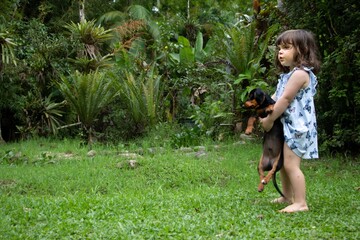 Garotinha, ao ar livre, junto à natureza, brincando com um cãozinho