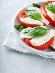 Italian Caprese Salad with sliced tomatoes, mozzarella and basil on white plate. Close up
