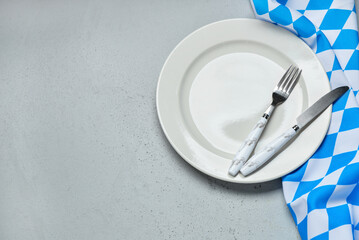 Empty plate, fork, knife and blue checkered tablecloth on grey table