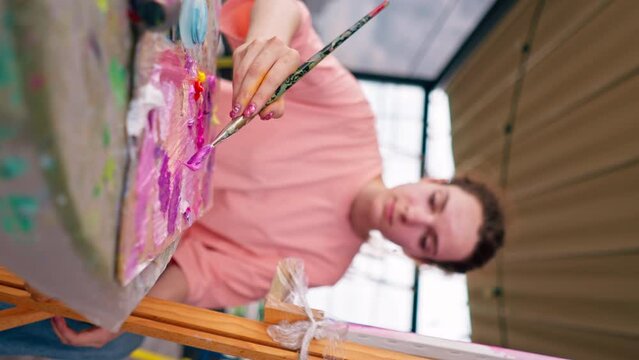 A girl artist with problem skin sits at an easel and paints a picture with a brush in her studio vertical