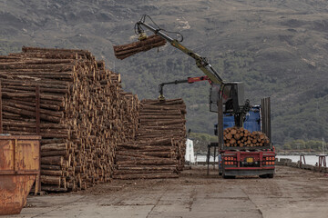 Fototapeta na wymiar Lorry with a grab taking wood off and piling it by a railway track