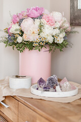An elegant bouquet of fresh roses, peonies, and daisies in a pink box, beautifully arranged and placed by a light-filled window.