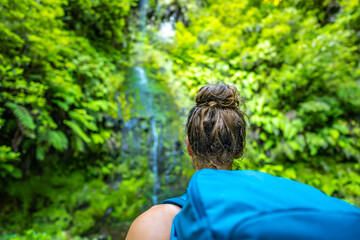 Backpacker tourist looking at green overgrown rainforst water fall. Levada of Caldeirão Verde, Madeira Island, Portugal, Europe.