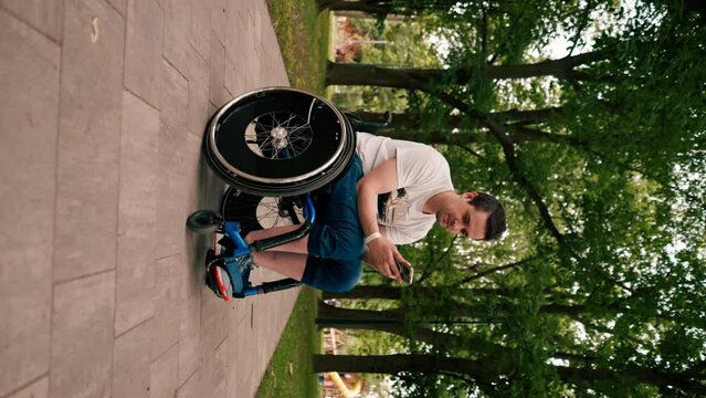 vertical video man in a wheelchair looks intently at the phone emotionally reads the news in the city park technology mobility