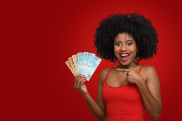 woman holding money, young smiling woman holding brazilian money. on red background