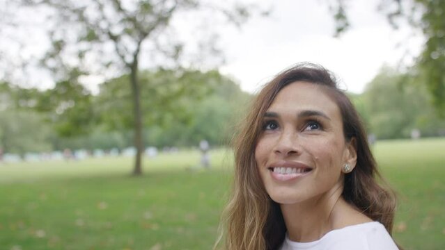 Attractive young woman walking in a park as she looks around smiling, in slow motion 